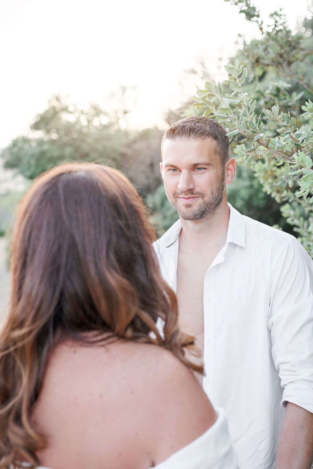 A romantic outdoor photoshoot showing a couple on a sandy path surrounded by lush greenery.