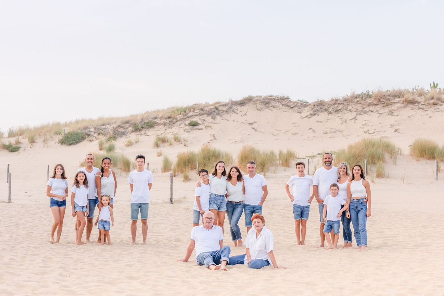 Extended family group poses together on sand dunes wearing coordinated casual outfits.