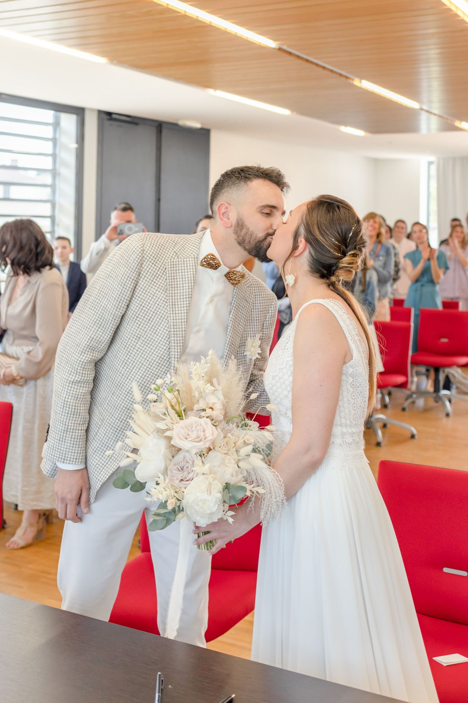 Wedding party in white and cream attire stands at altar during indoor ceremony.