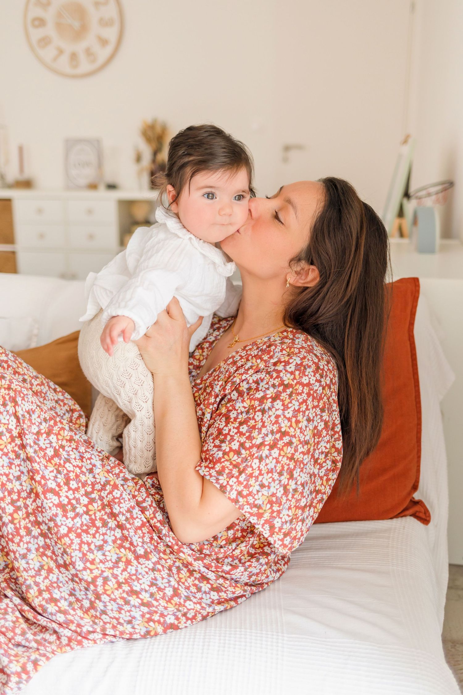 A tender moment shared on white bedding with someone wearing a floral dress holding a baby in white.