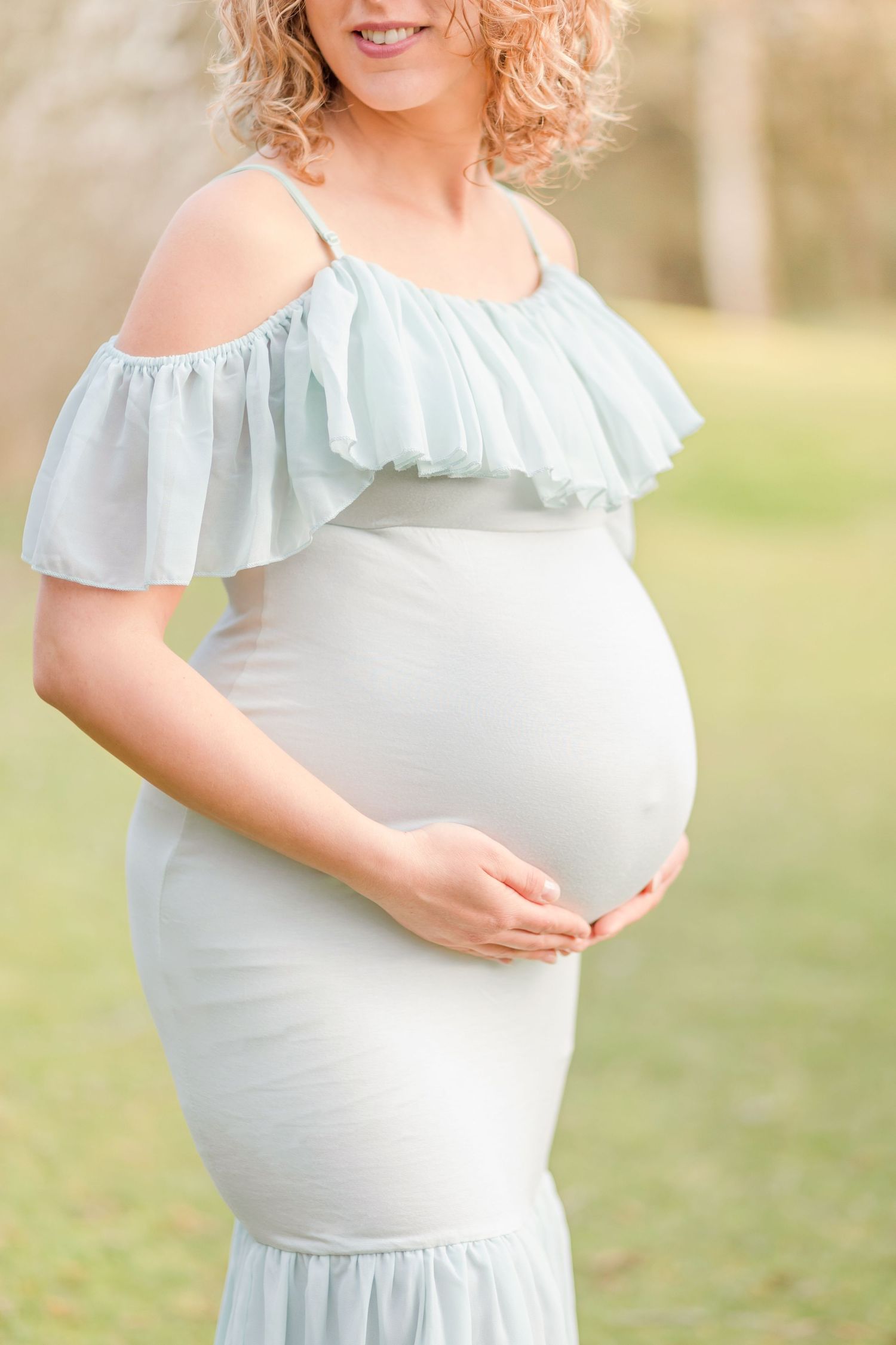 Close up of maternity bump in pale blue ruffled dress outdoors.