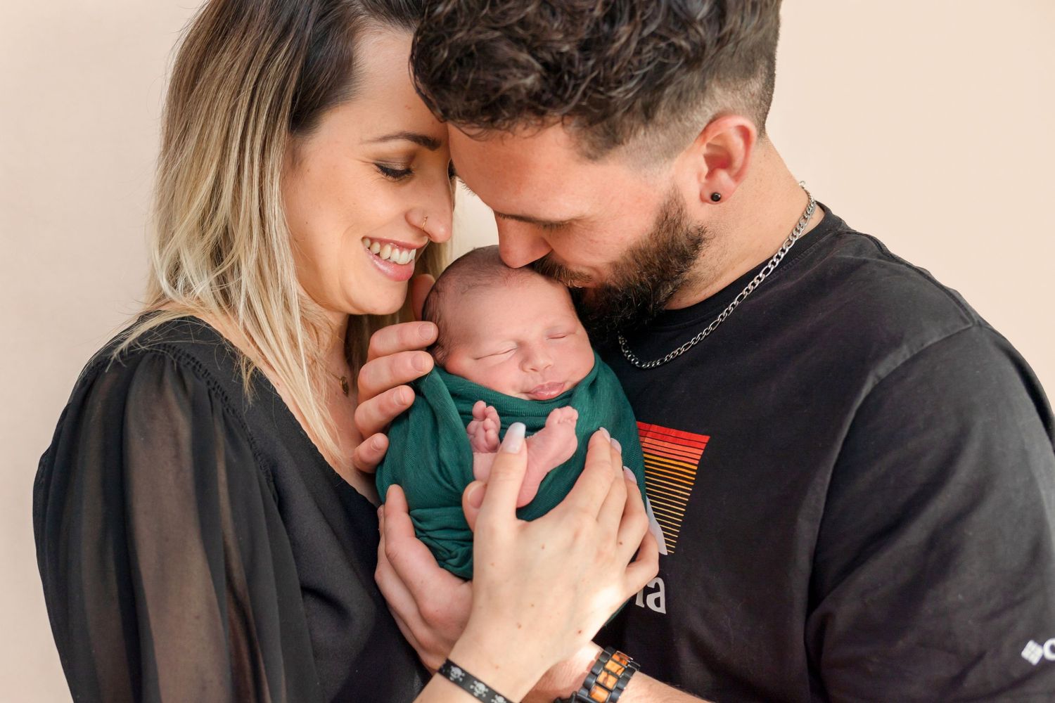Intimate family portrait showing parents sharing a joyful moment with their swaddled newborn.
