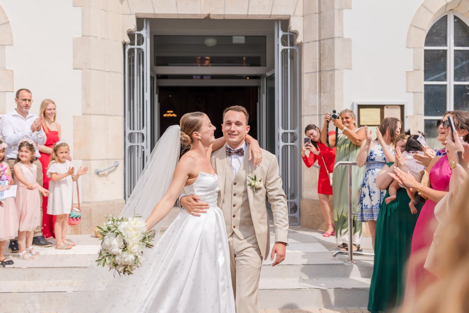 Joyful newlyweds celebrate outside church steps surrounded by wedding guests.