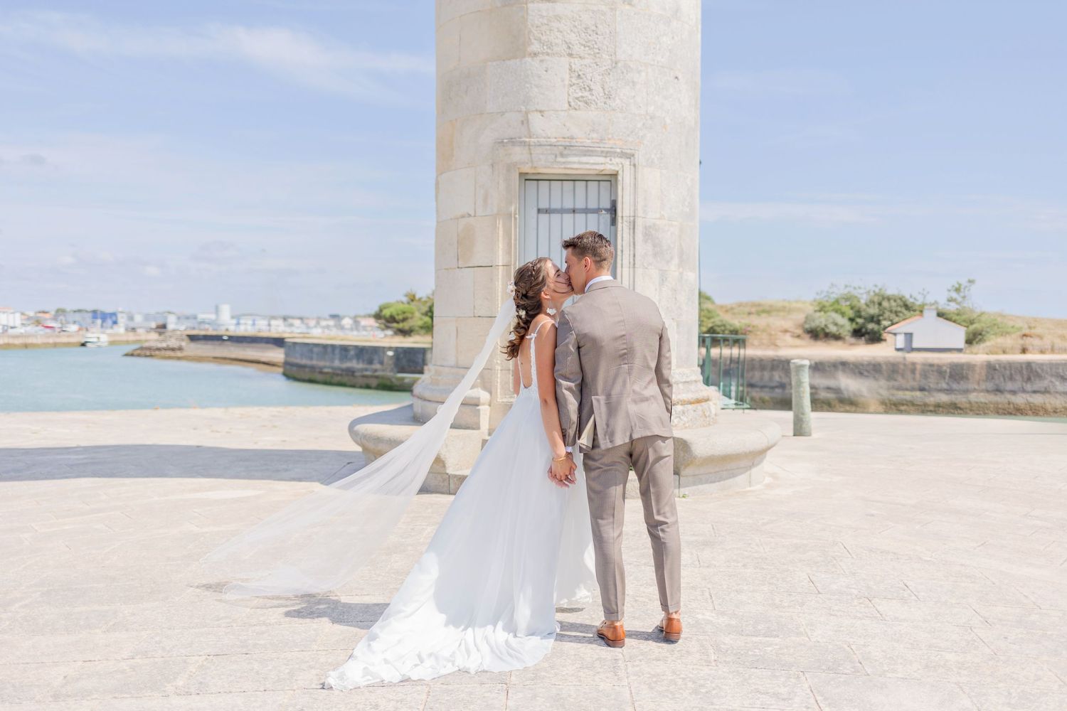 Wedding couple sharing intimate moment near base of coastal lighthouse.