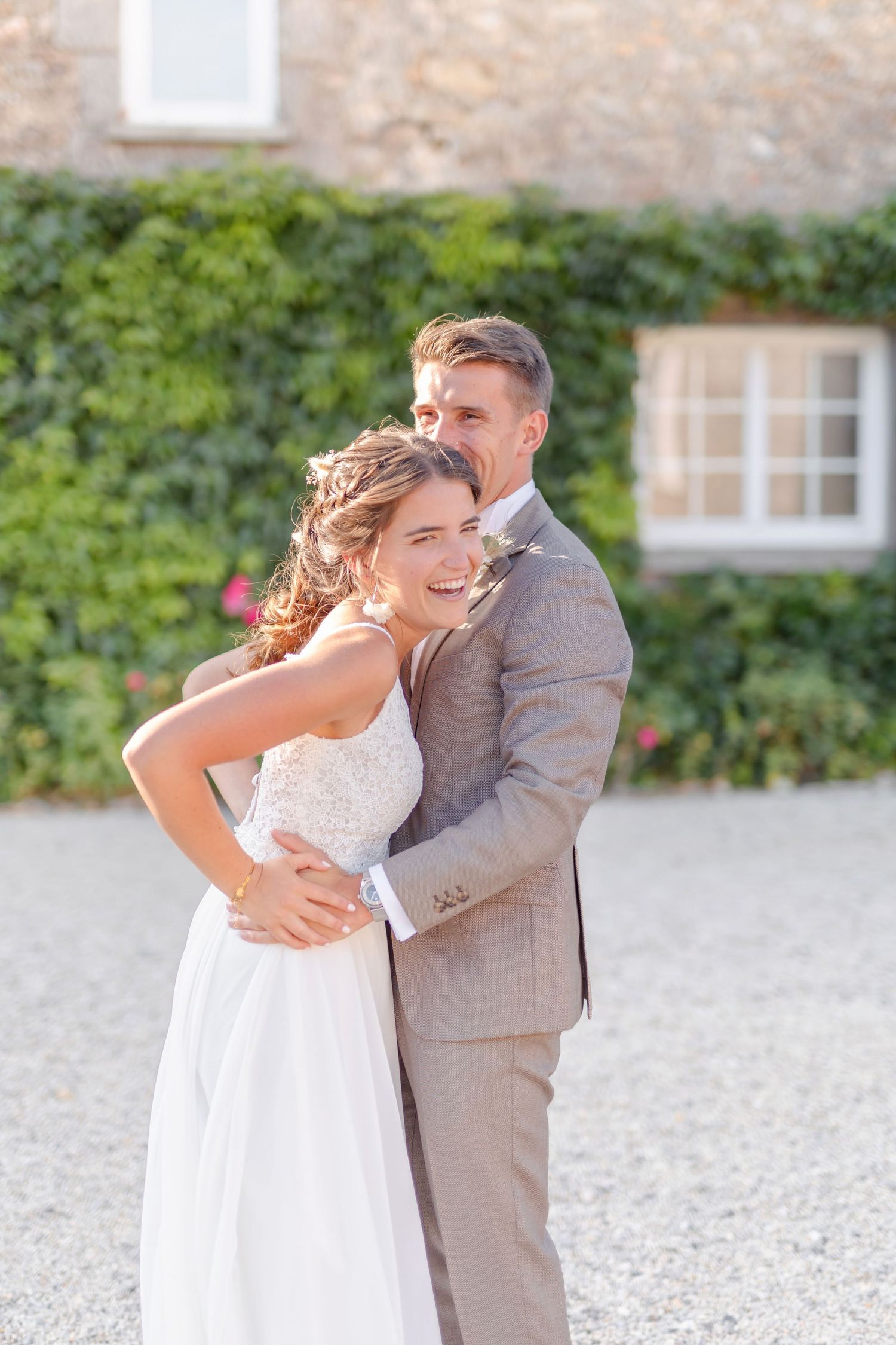Joyful newlyweds share a candid moment together against a rustic stone building backdrop.