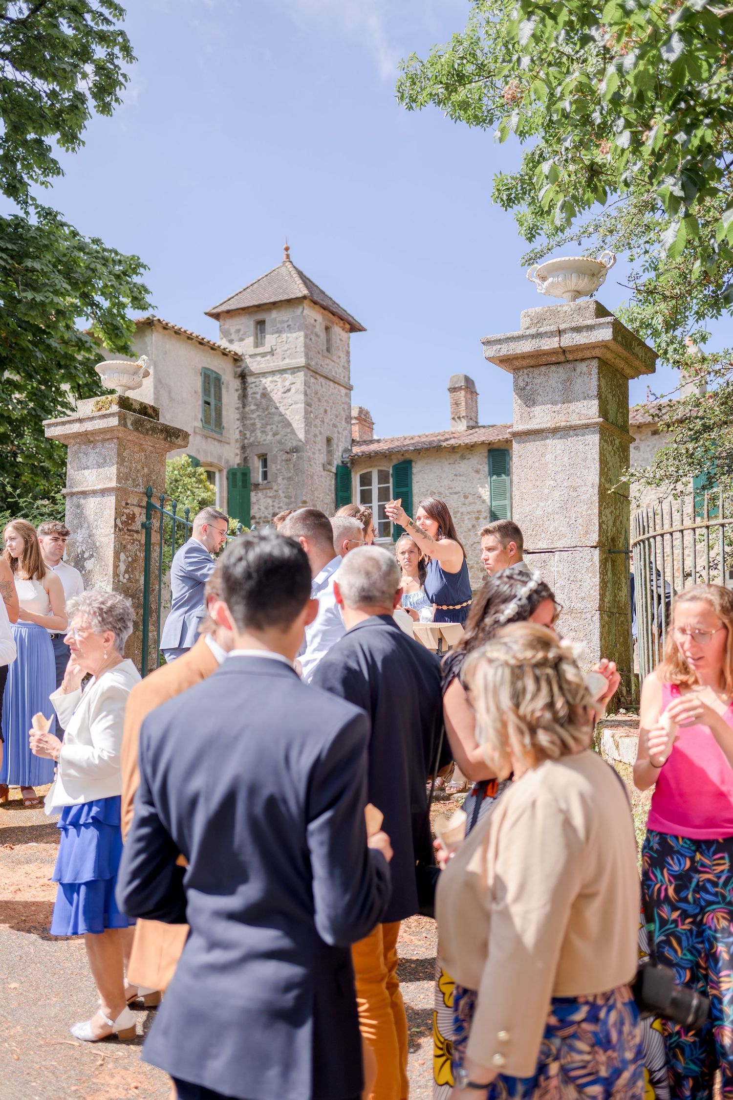 Wedding party and guests gathering outside historic stone building entrance.
