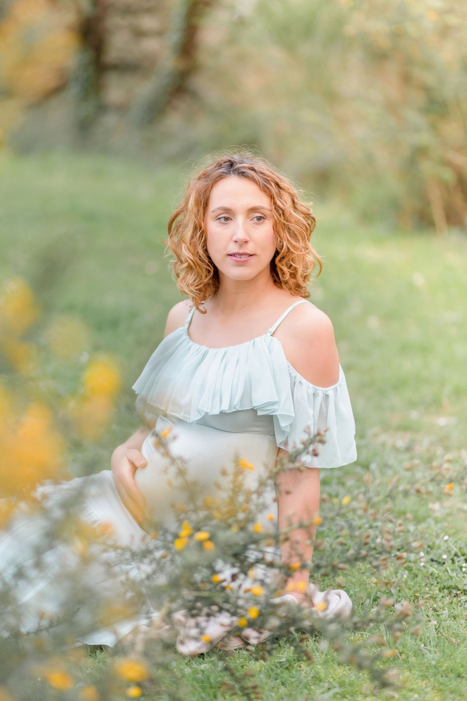 A dreamy outdoor portrait showing a woman in a light blue off-shoulder dress surrounded by nature.