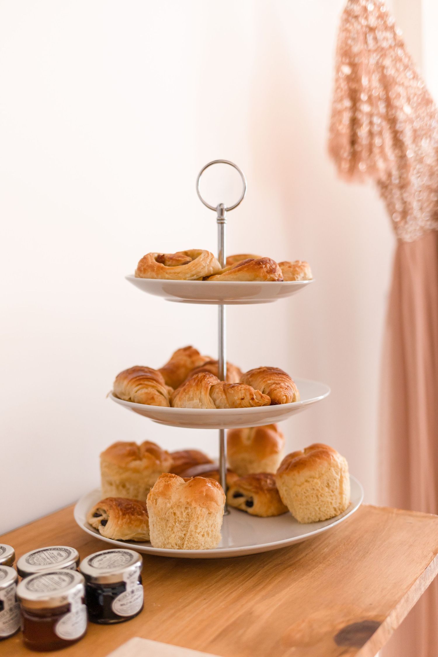 Three-tiered serving stand with fresh pastries and croissants on wooden table.
