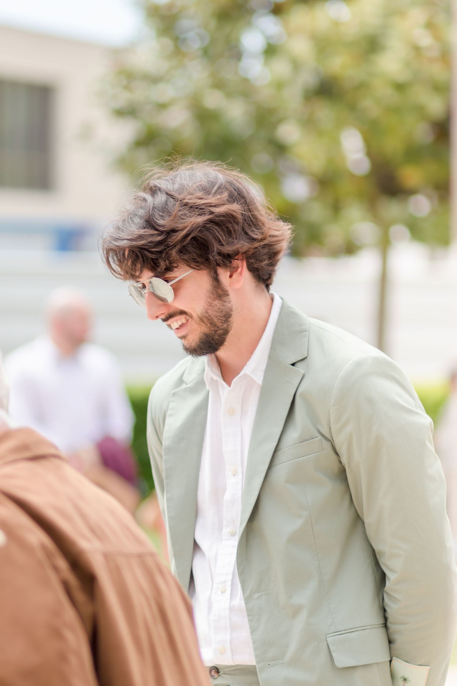 Guest in mint green blazer and white shirt smiles during outdoor wedding festivities.