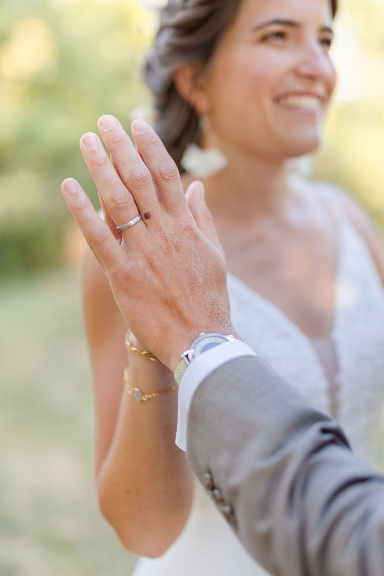Close-up of wedding rings and hands against blurred natural background.