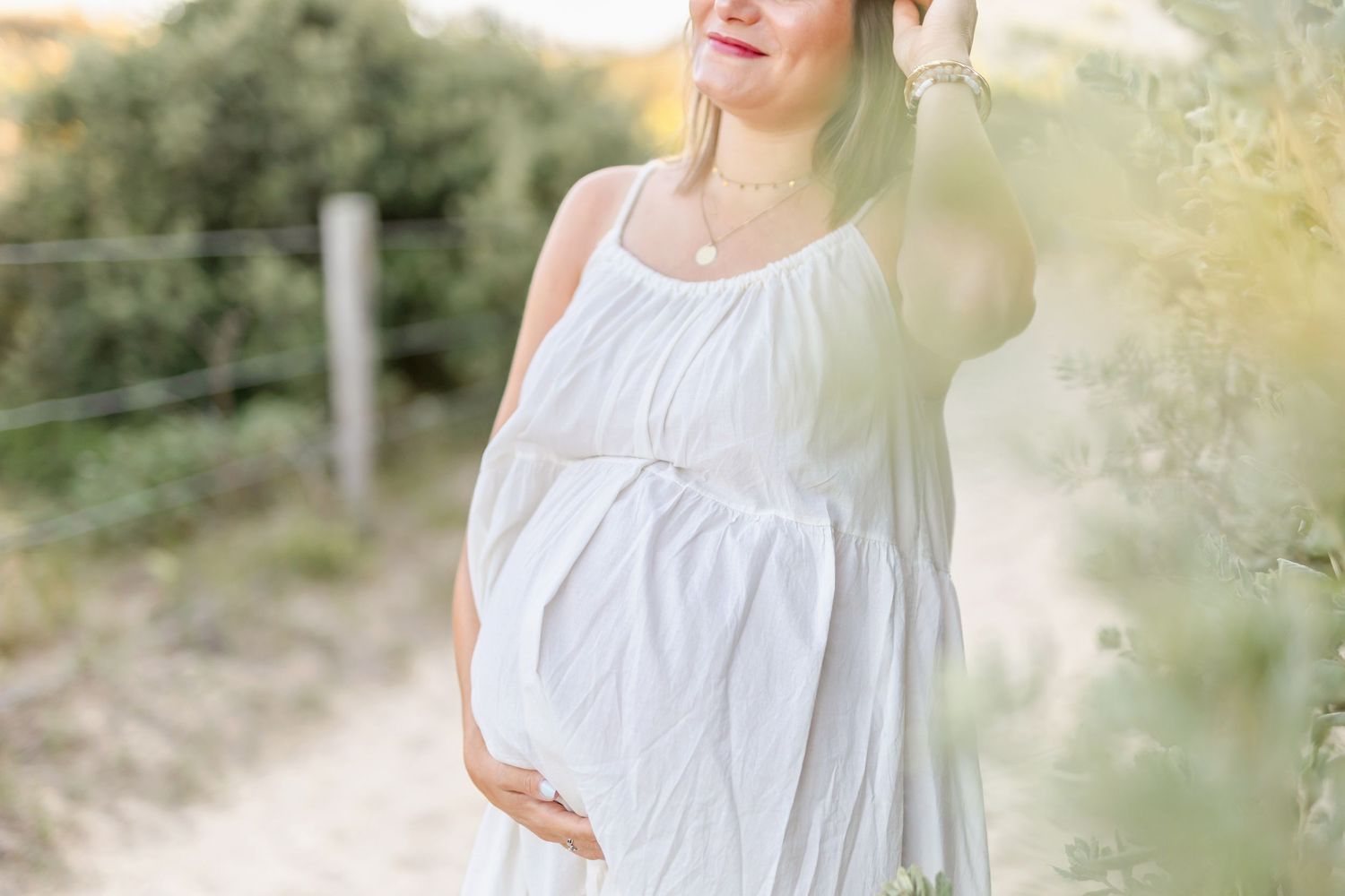 Expectant mother in flowing white dress poses on outdoor path during sunset.