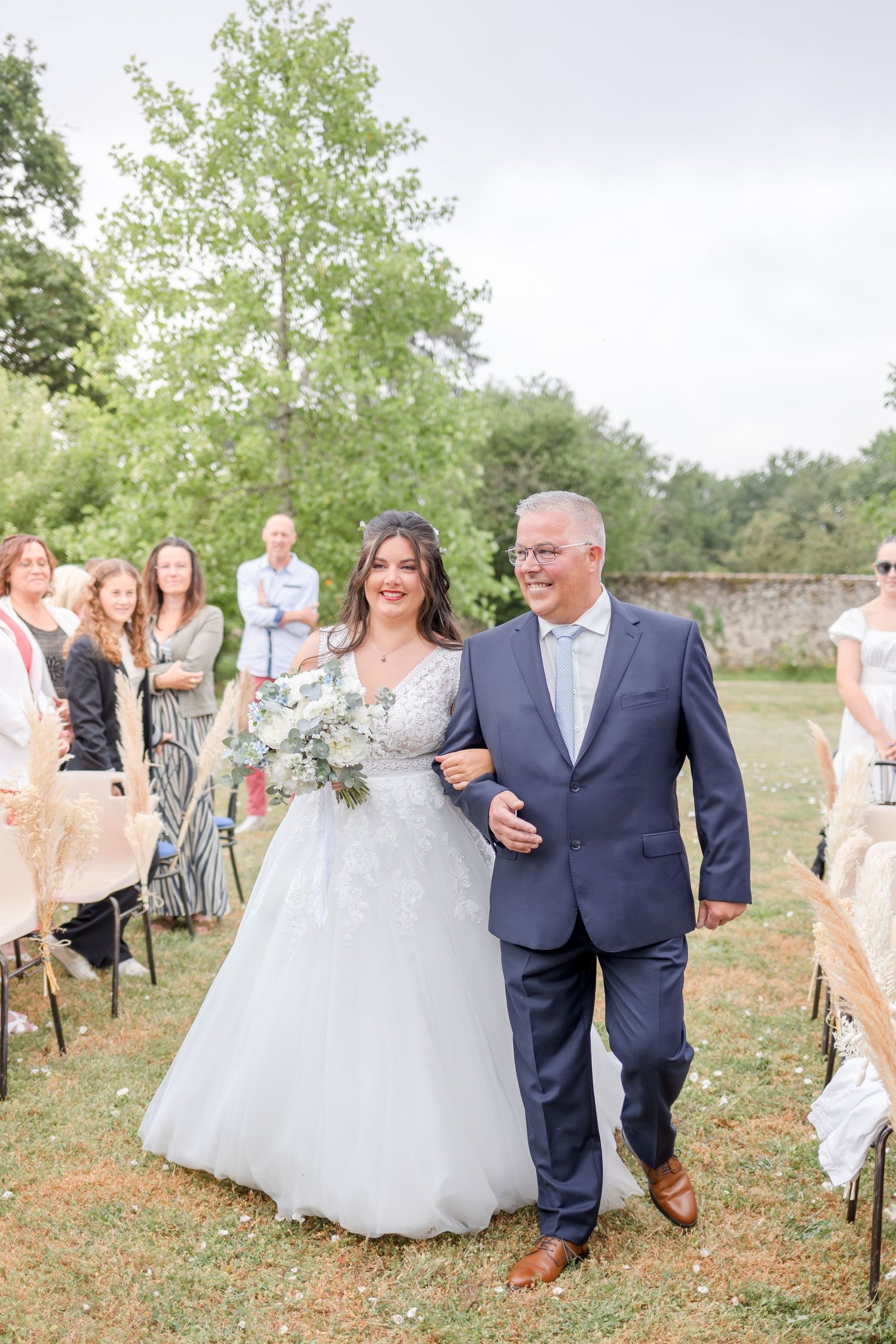 Outdoor wedding ceremony with guests gathered on a grassy lawn surrounded by trees.