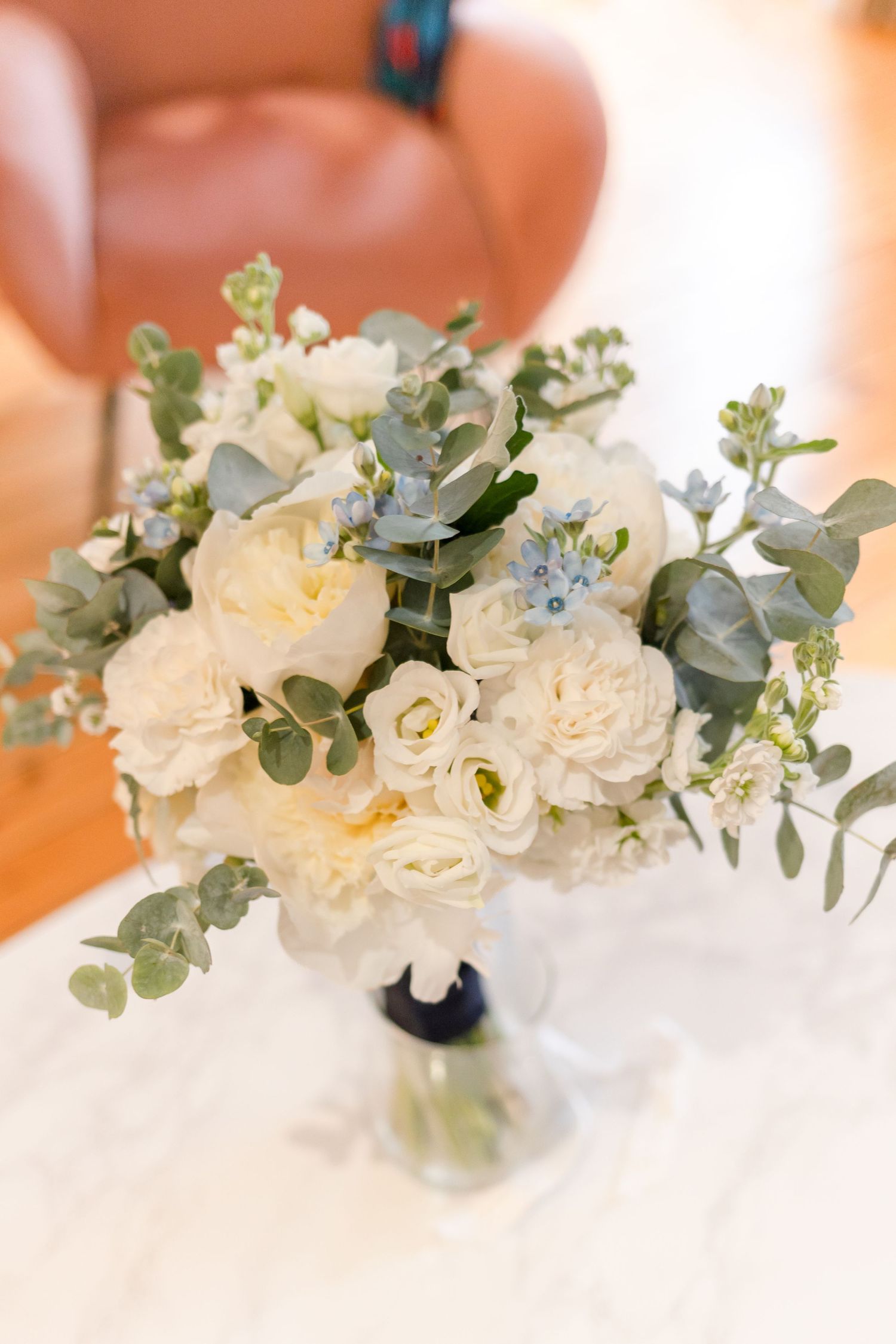 Elegant white wedding bouquet with roses, eucalyptus, and delicate blue accents in glass vase.
