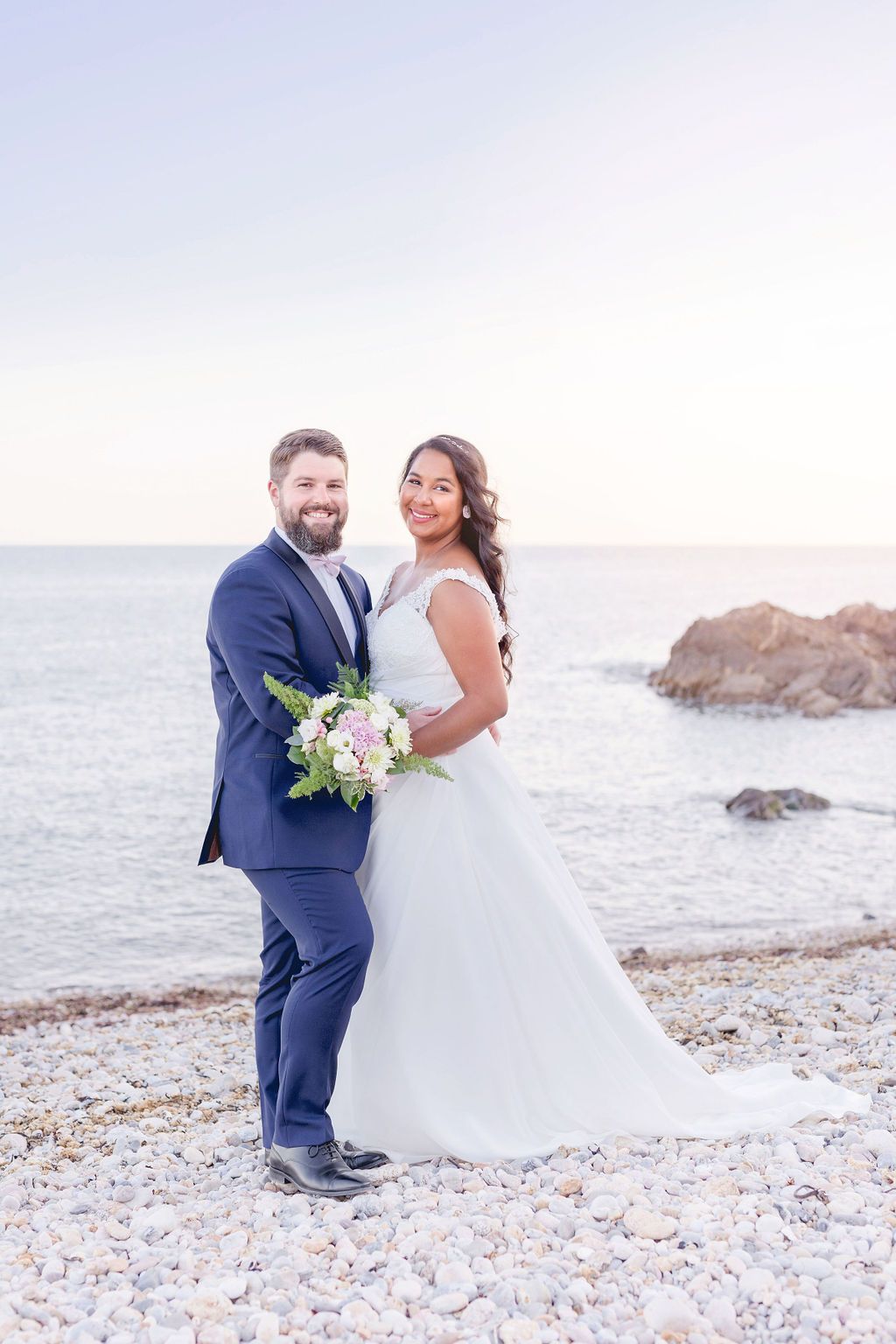 A romantic beach wedding portrait with white floral bouquet against coastal backdrop.