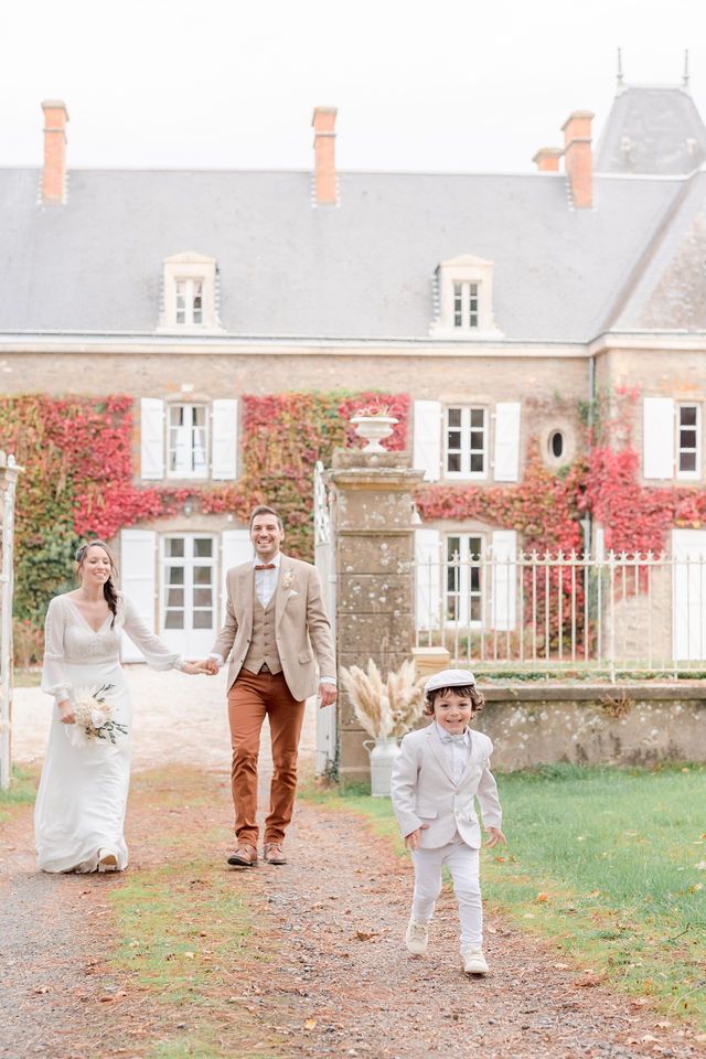 Family portrait on a path leading to a beautiful stone mansion with red autumn foliage.
