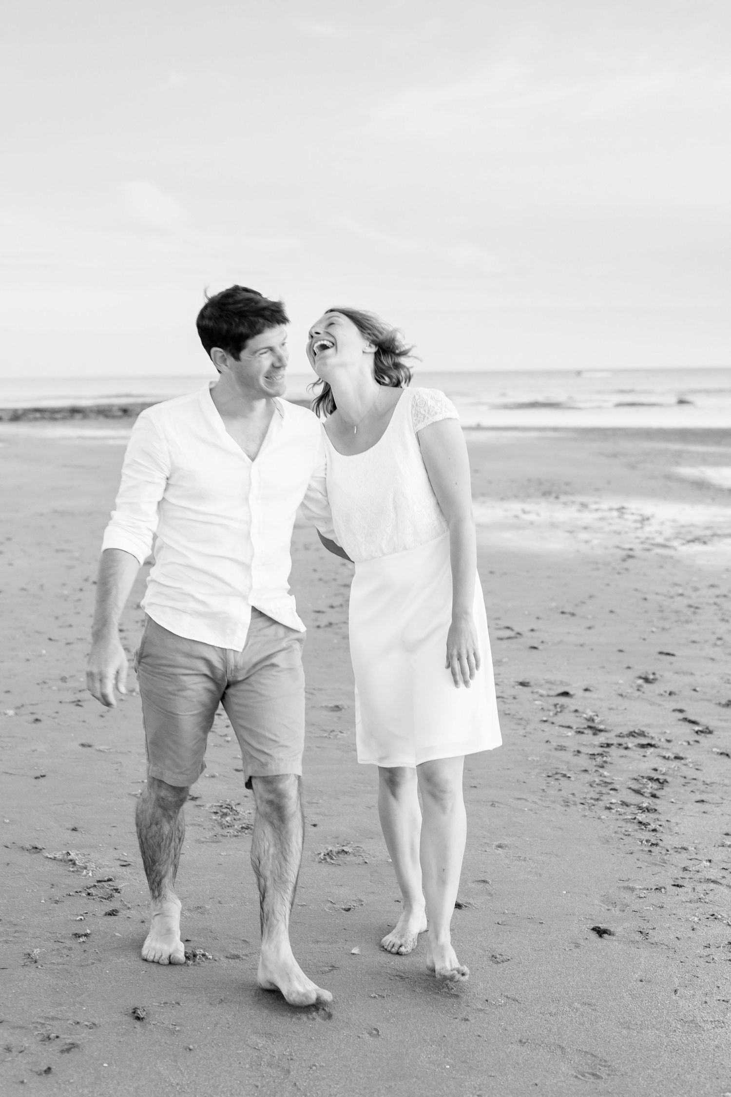 A black and white photo captures a couple walking intimately along a peaceful beach.