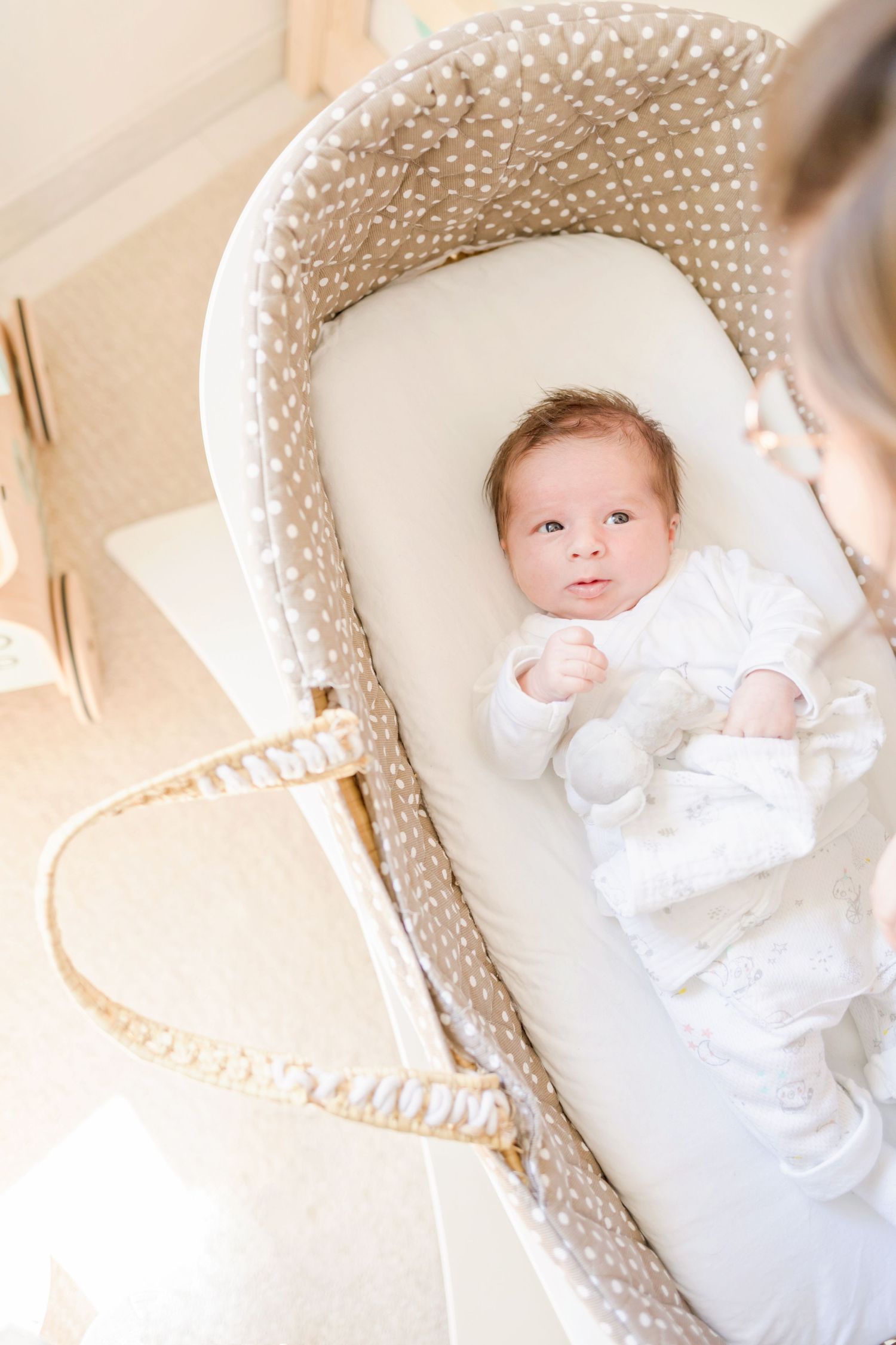 Infant lying in cozy beige polka dot bassinet with white padding.