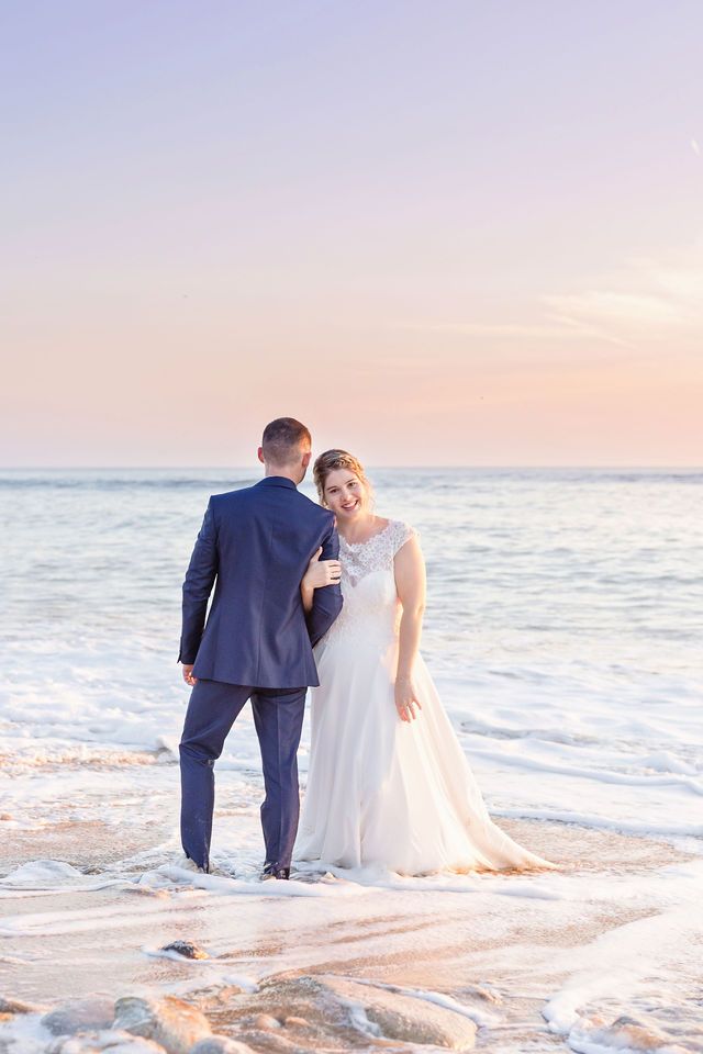 A couple shares an intimate moment on the beach at dusk in their wedding attire.