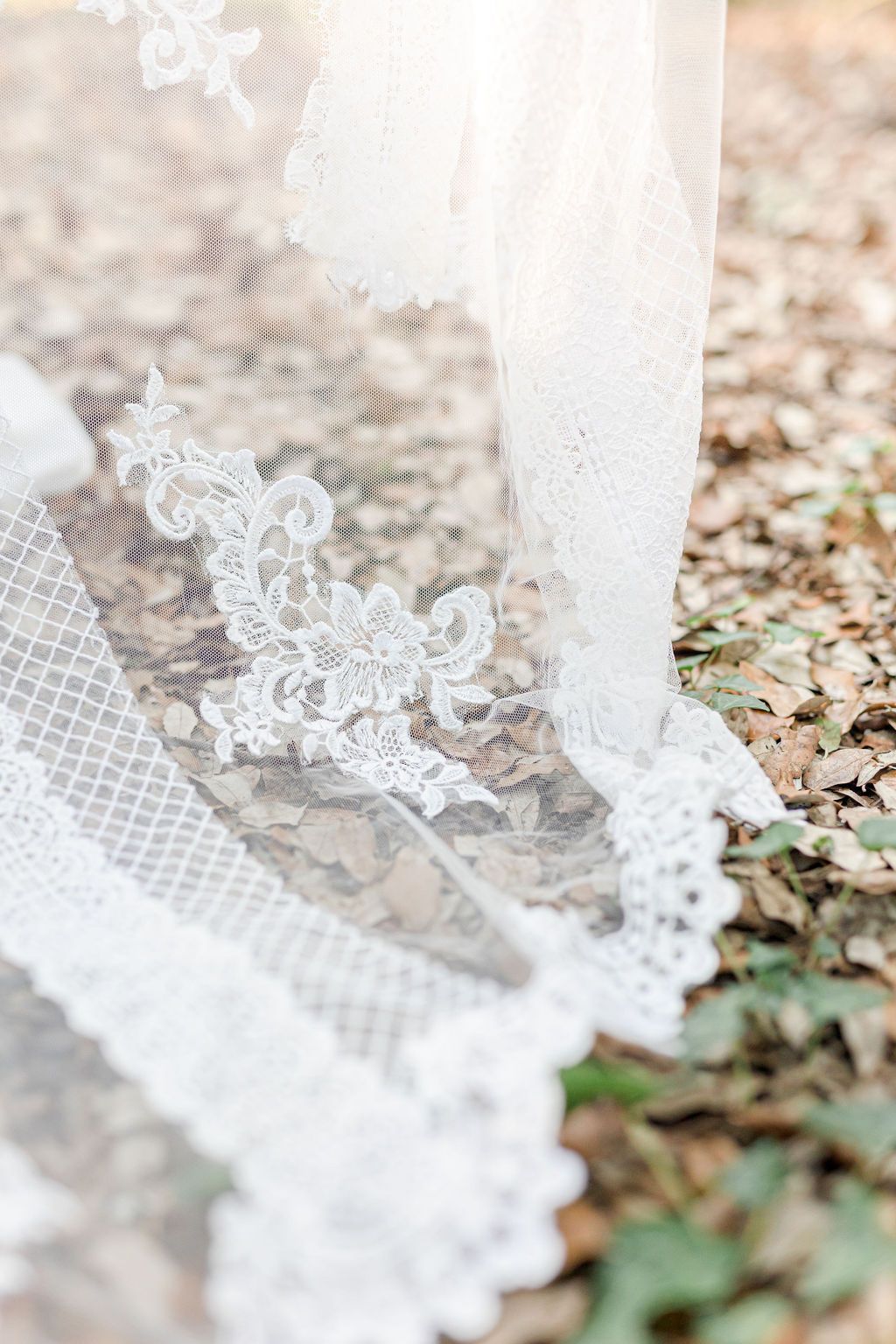 Delicate lace detail on white wedding dress train against forest floor.