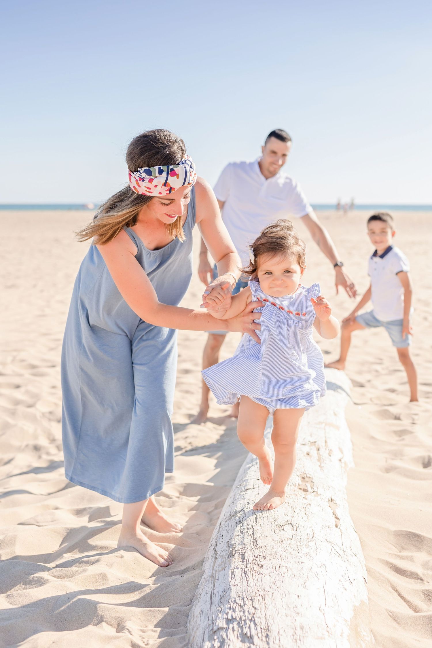 Family enjoying a playful moment on a sandy beach wall on a bright sunny day.