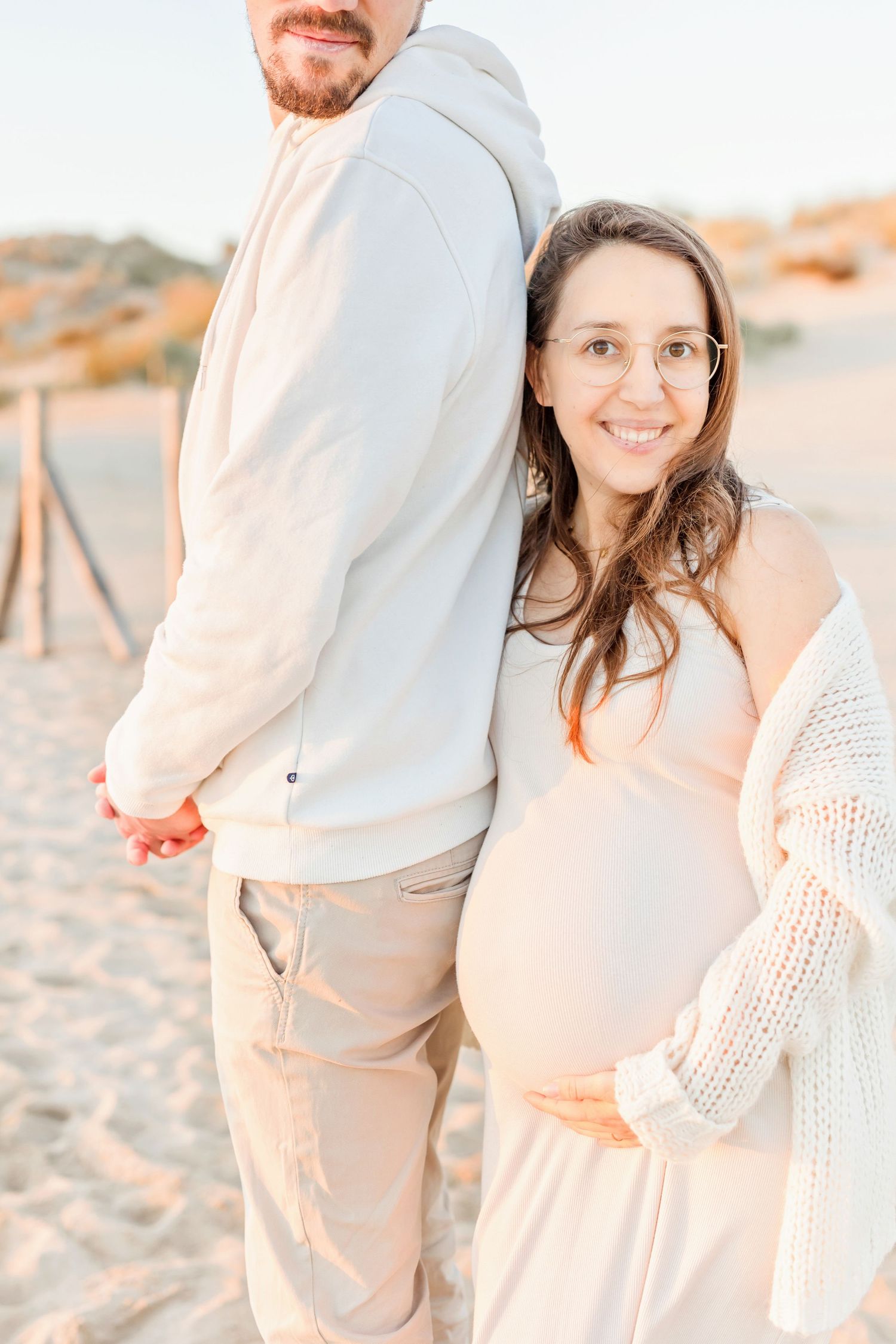 A couple in neutral tones shares tender moments on a beach at sunset.