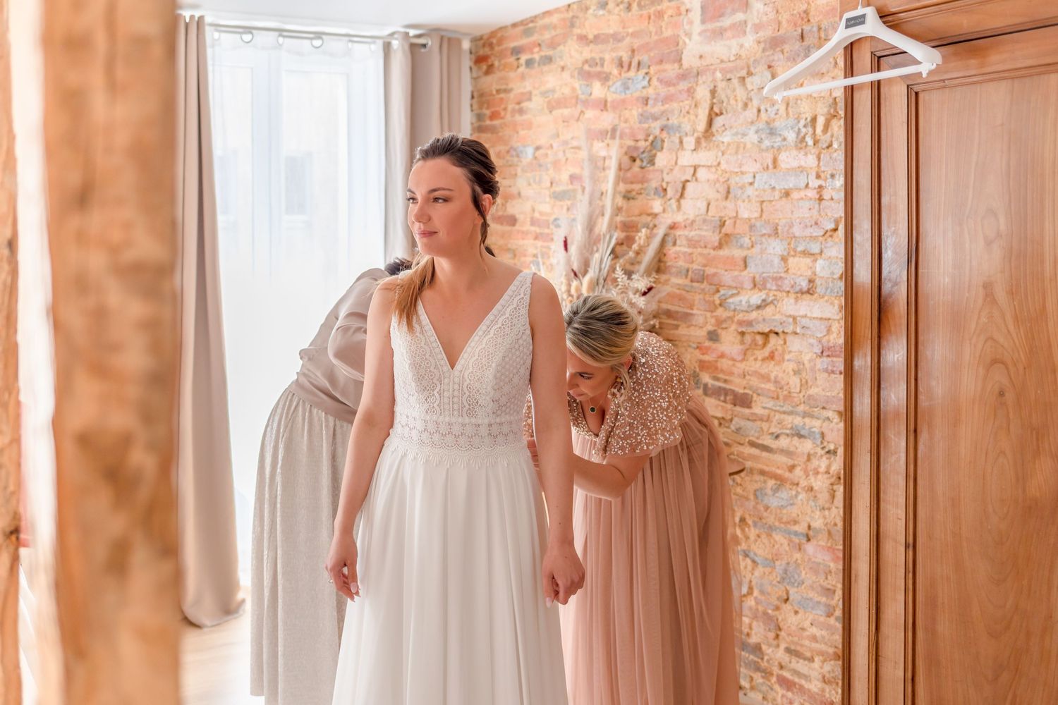 Elegant bride in white dress standing in rustic room with exposed brick walls.