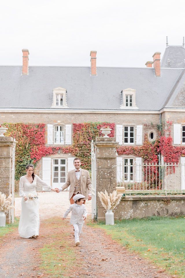 Happy family walking on a gravel path in front of a historic French manor with autumn vines.