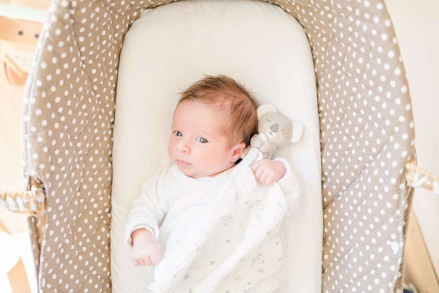 Baby resting in polka dot bassinet wearing white clothing.