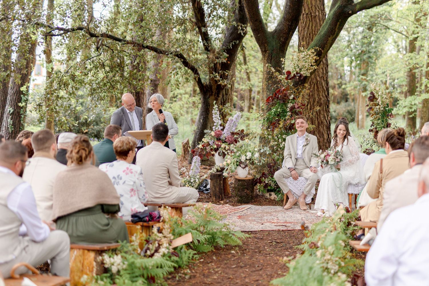 Wide panoramic view of wedding guests seated in a wooded outdoor ceremony space.