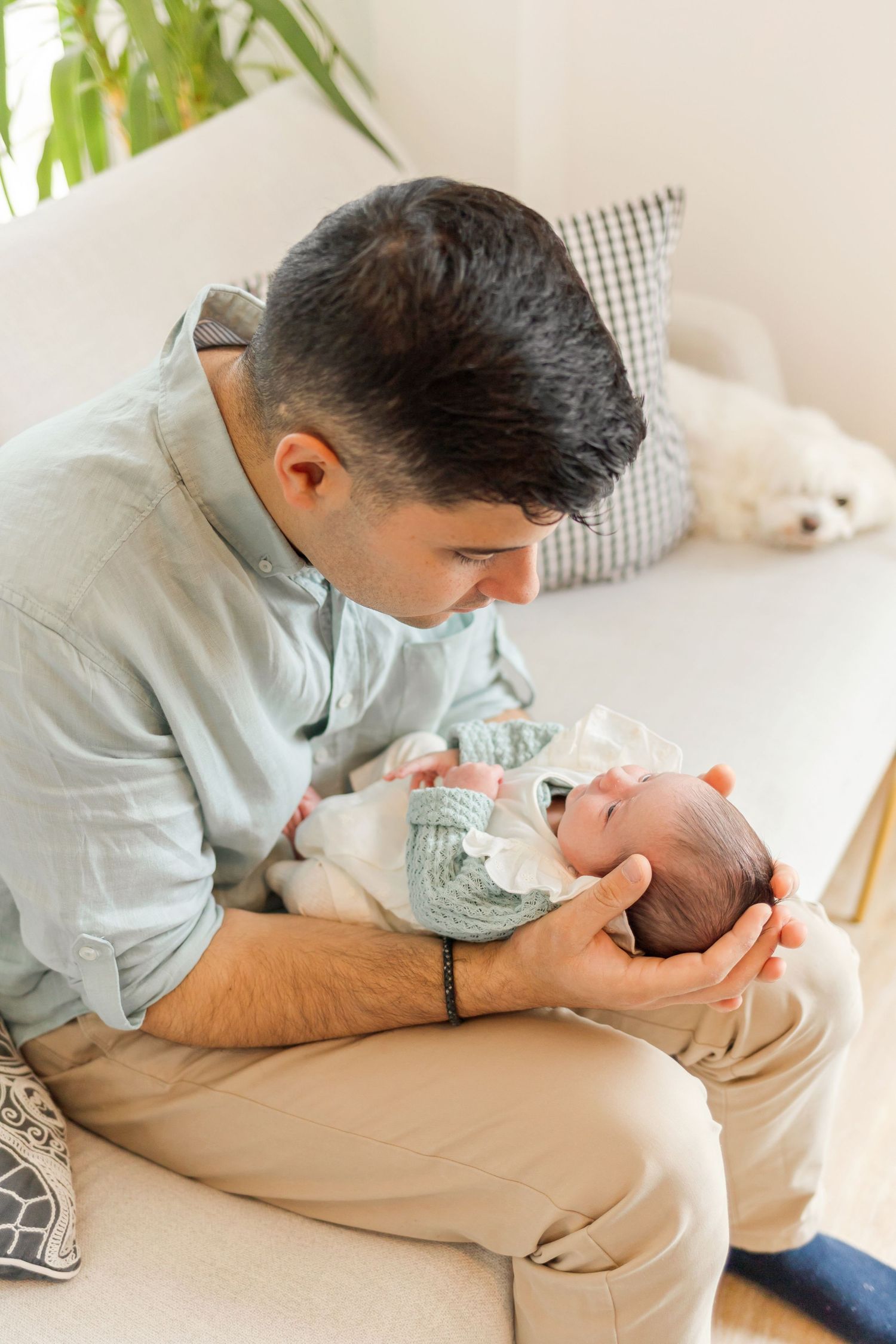 Parent in light blue shirt tenderly holding newborn baby on beige couch.