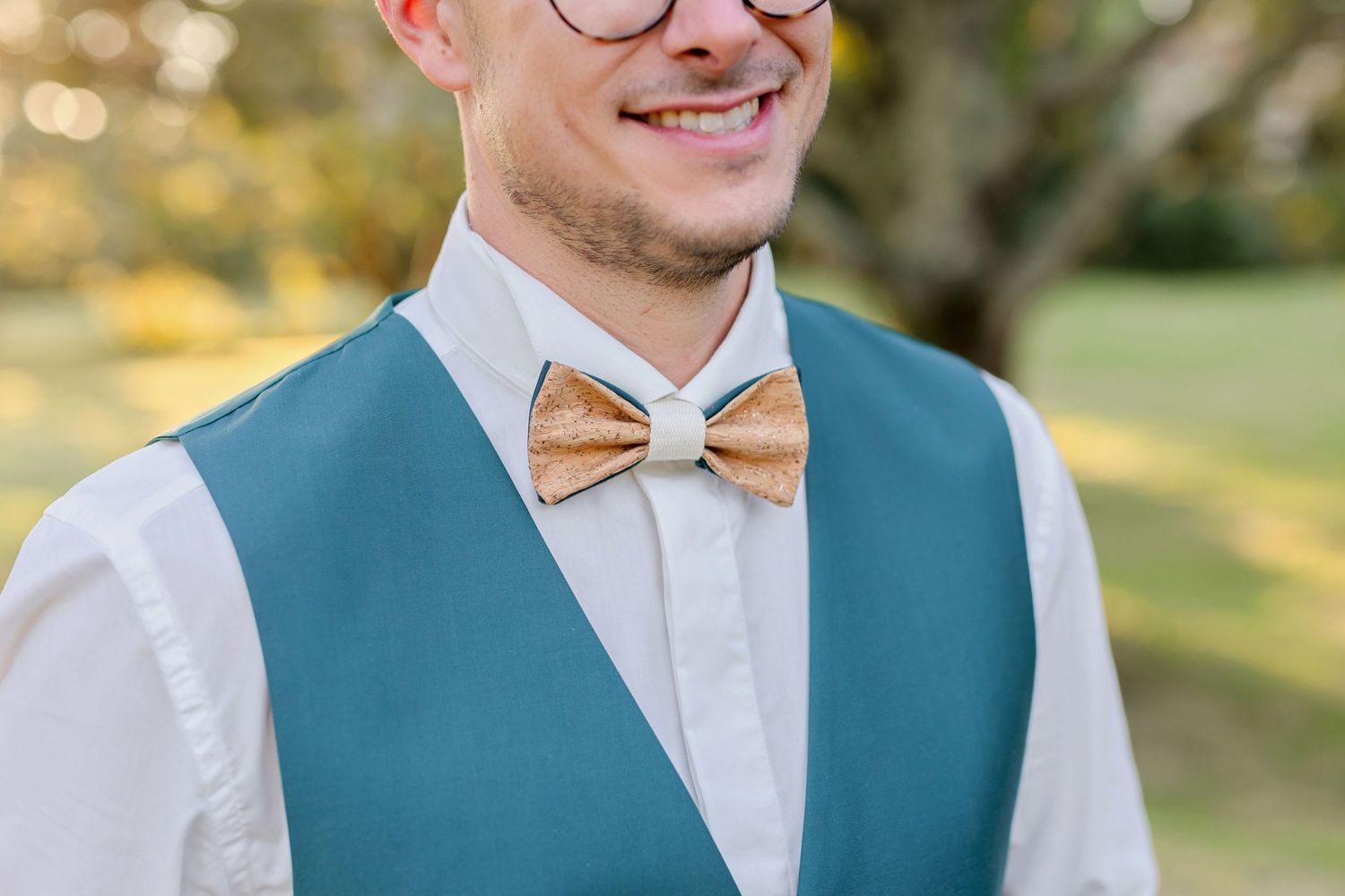 Close-up detail of a groom's teal vest and wooden bowtie with glasses.