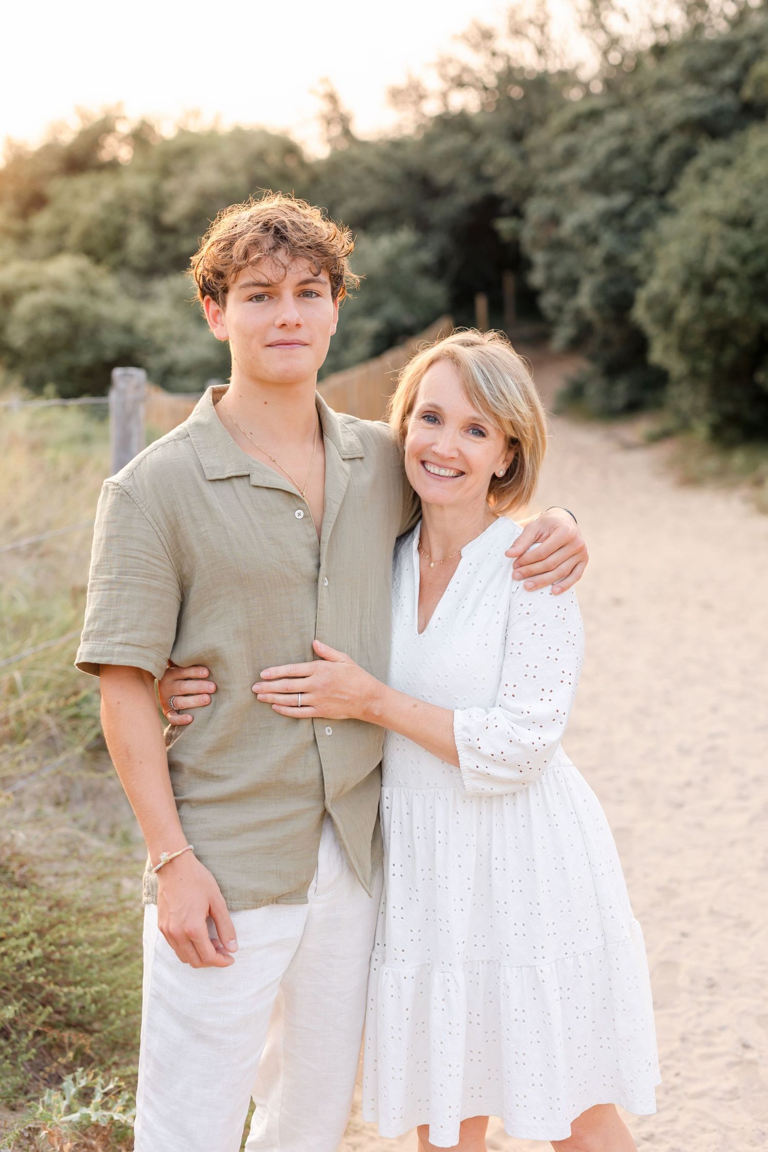 Two people in coordinating beige and white outfits embracing on nature path at golden hour.
