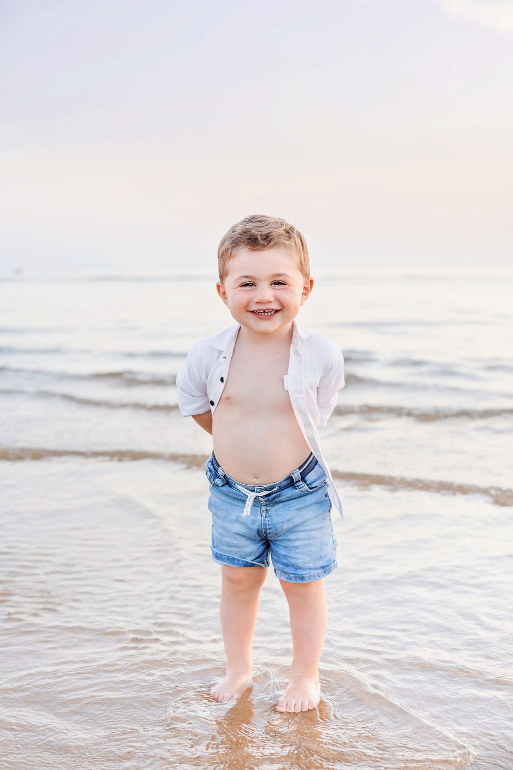 Child in denim shorts and white shirt playing in ocean waves at beach.