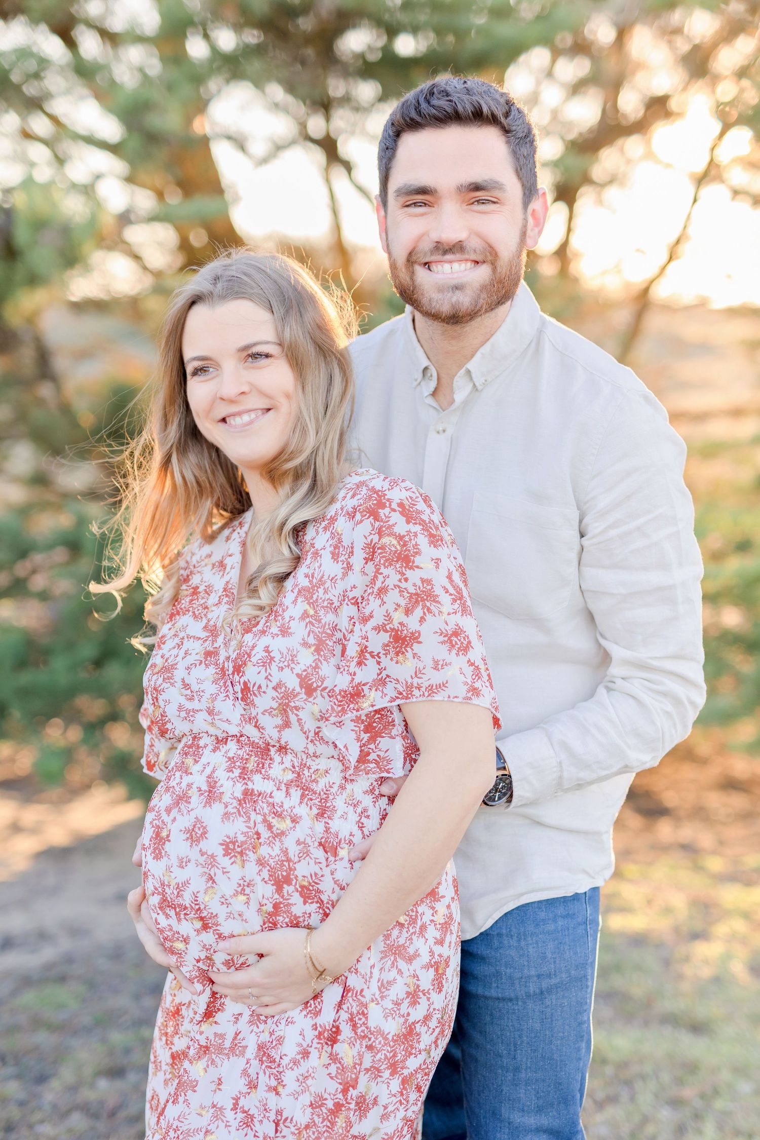 Joyful maternity photo of couple smiling in golden sunset light.