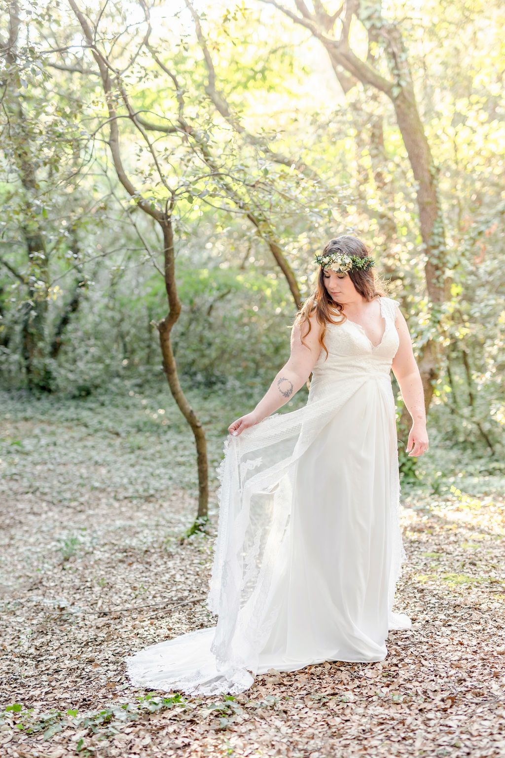 Bride in flowing white dress poses gracefully in ethereal woodland setting.