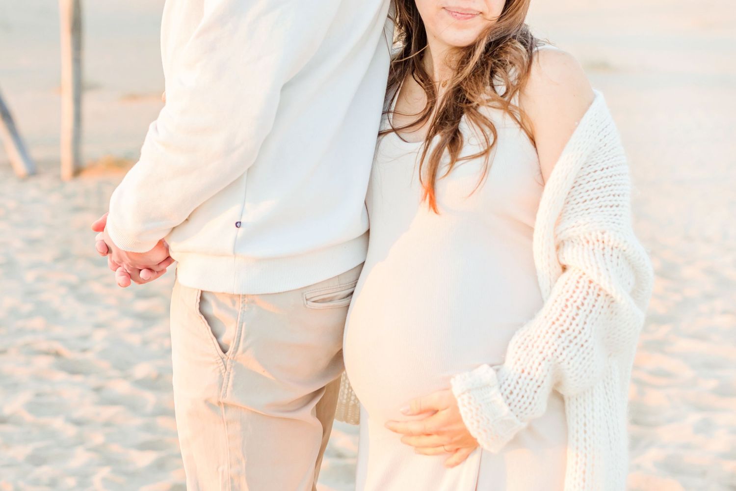 Two people in light colored clothing share an intimate moment on a beach at sunset.
