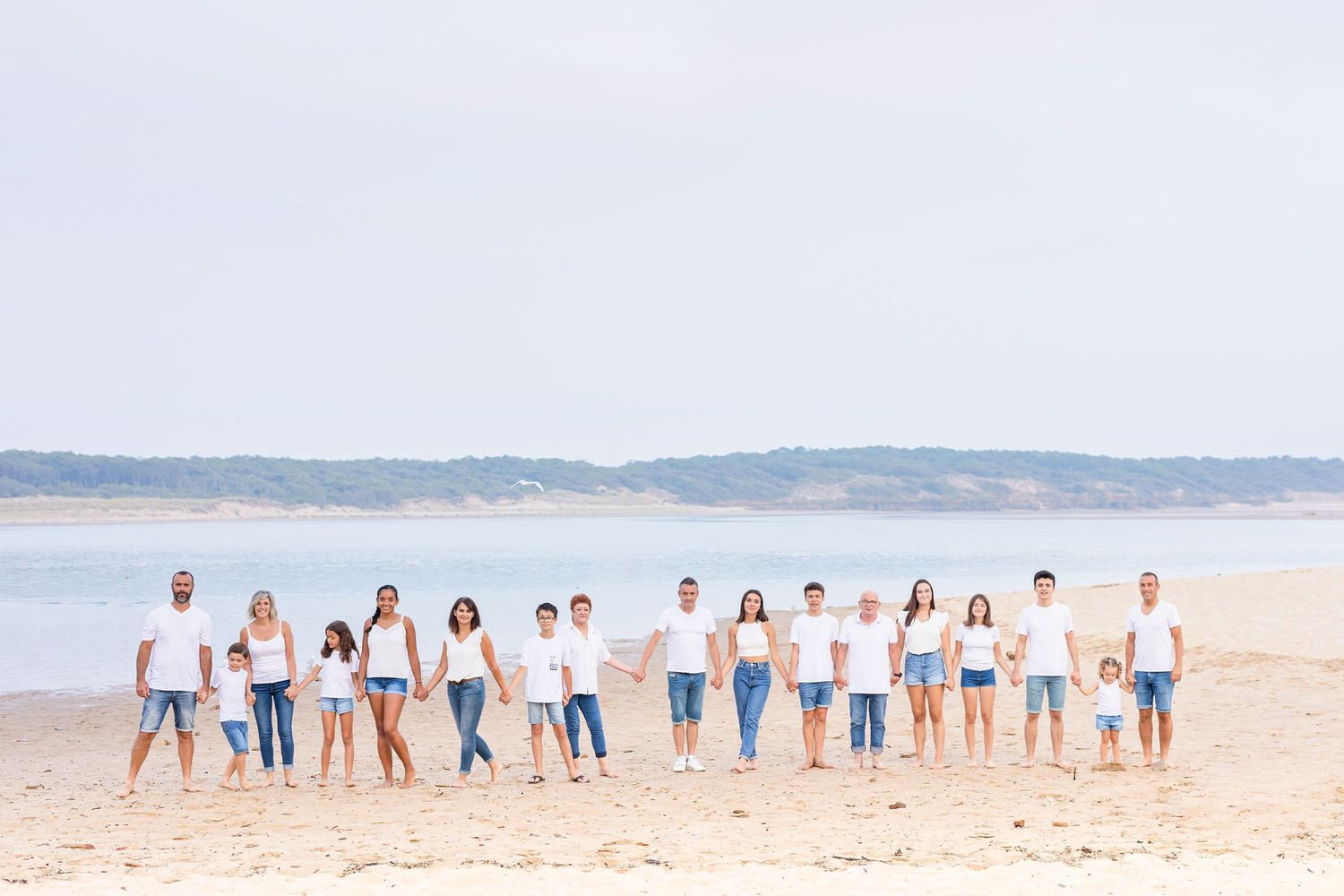 Wide landscape shot of family group lined up along shoreline wearing coordinated white and blue outfits.