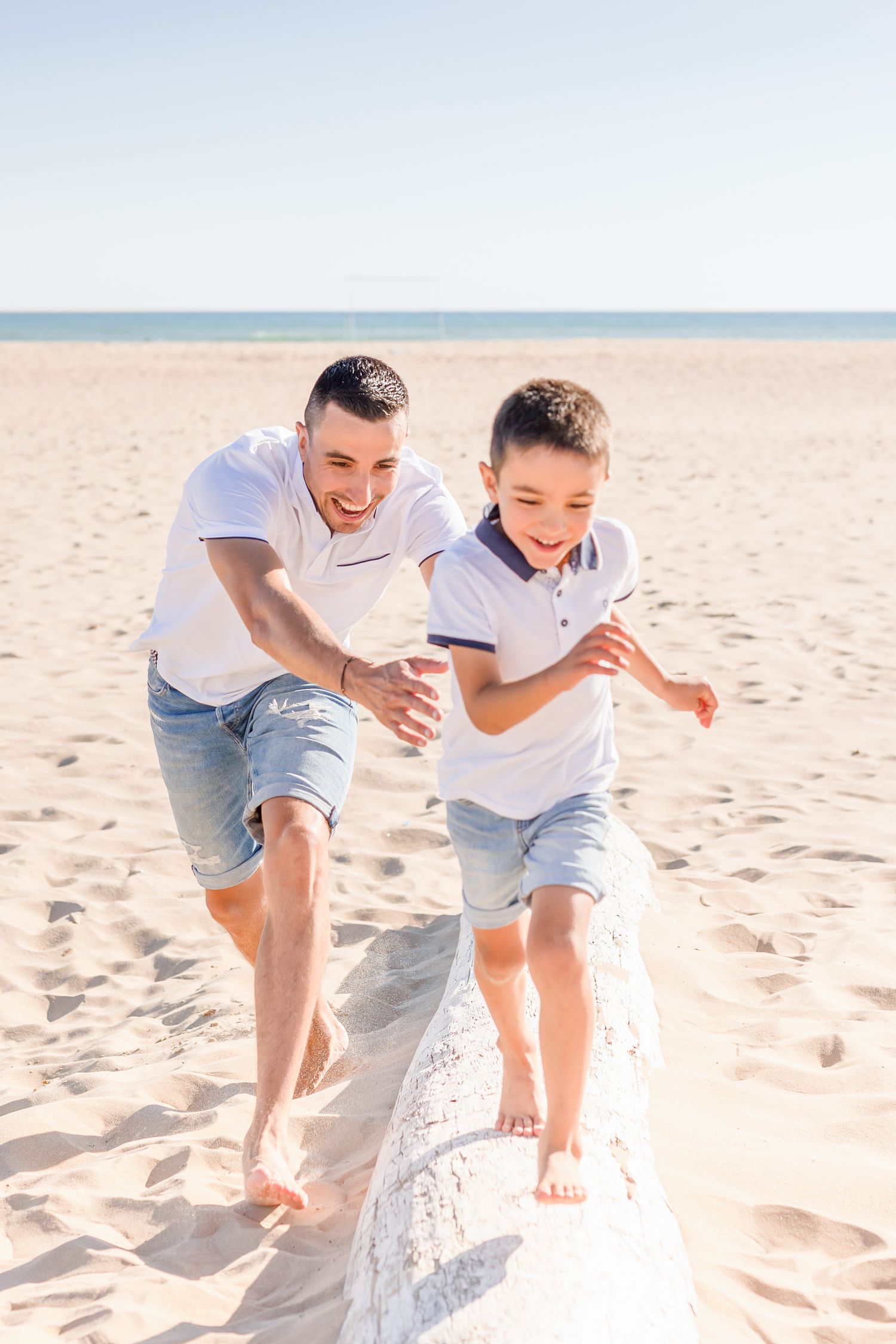 Father and son running together on sandy beach during golden hour photo session.