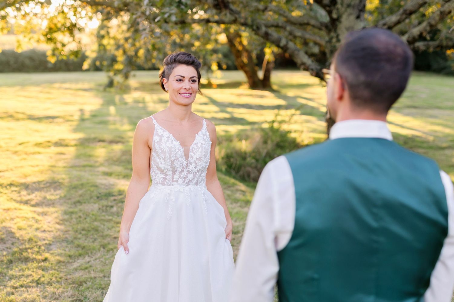 Bride in lace gown looks lovingly at groom in garden setting.