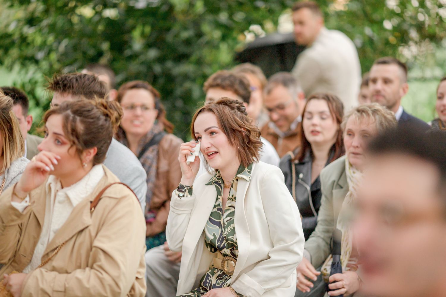 Wedding guests watch ceremony while seated outdoors in casual attire.
