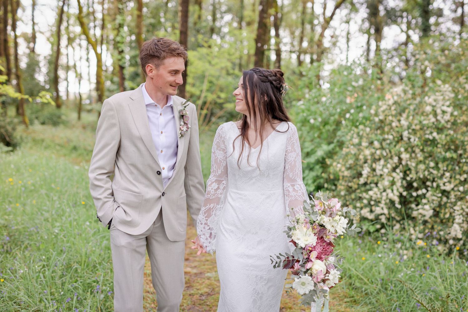 Newlyweds walking together on a nature path with the bride carrying a bouquet.