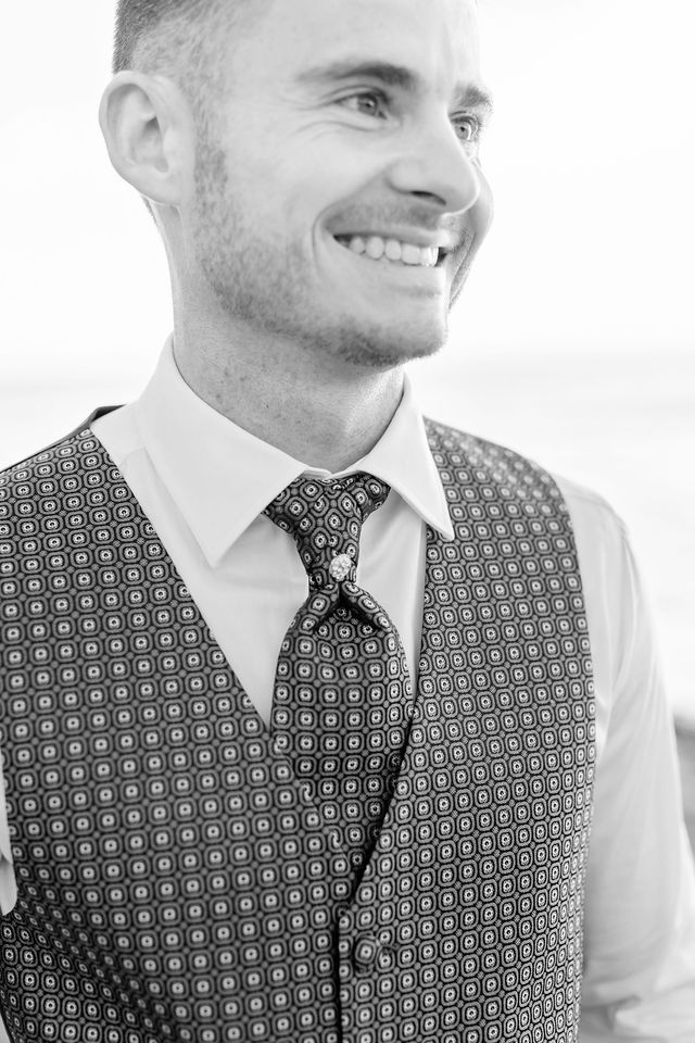 Groom wearing a patterned vest and tie smiles in black and white portrait.
