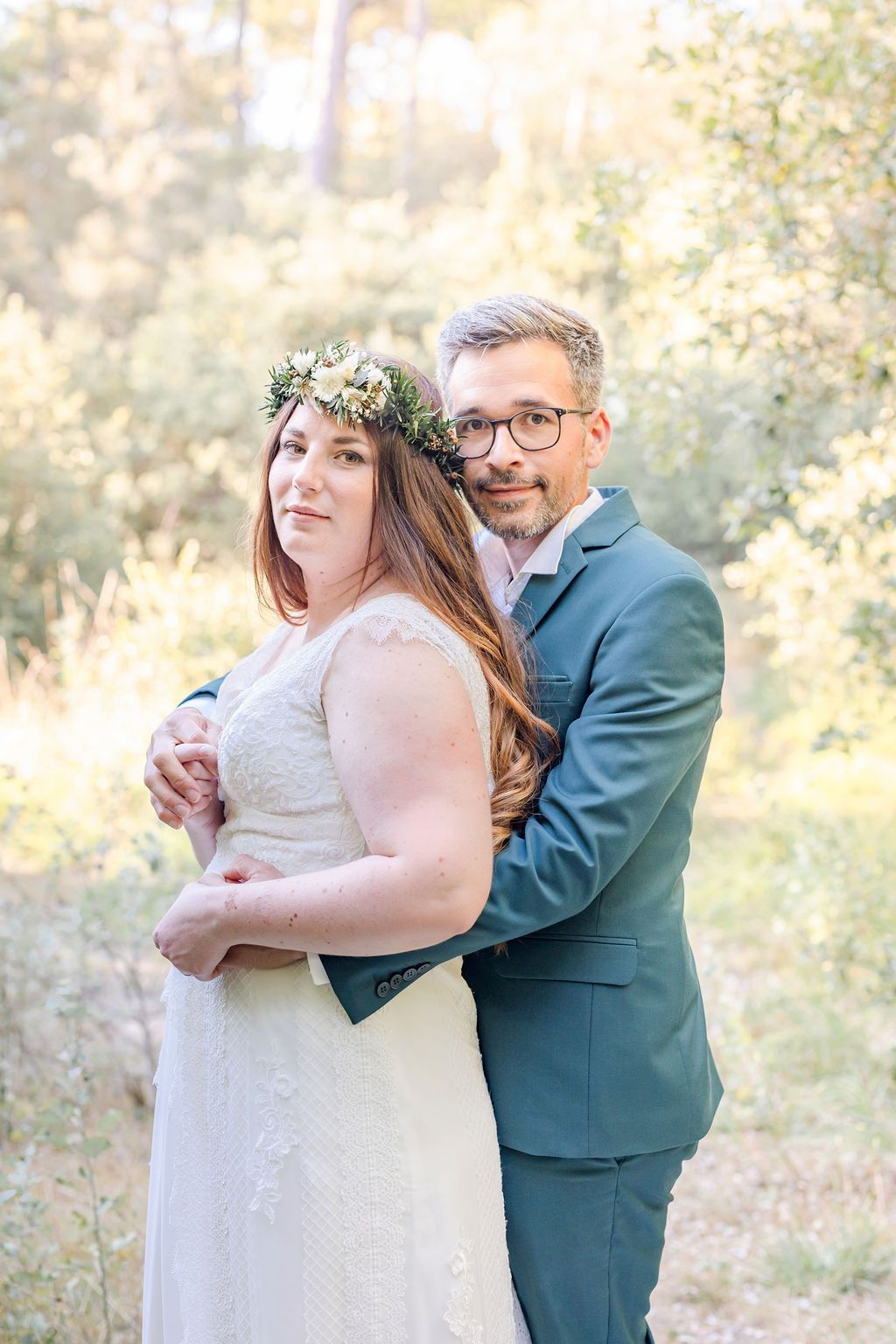 Joyful wedding couple sharing intimate moments in a sun-filled forest setting.