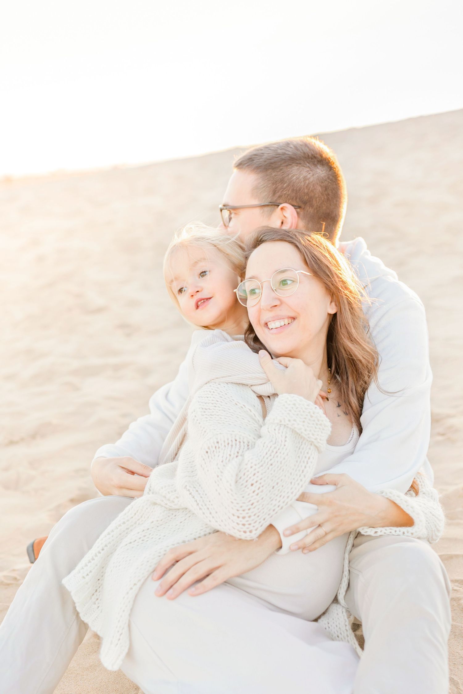 Family cuddles together on sandy beach during golden hour portrait session.
