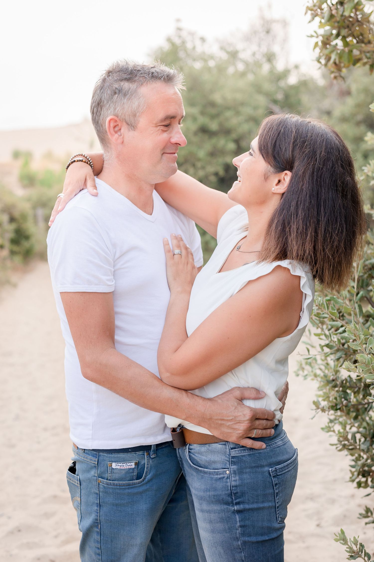 Intimate couples portrait showing tender moments in matching white tops and jeans against nature backdrop.