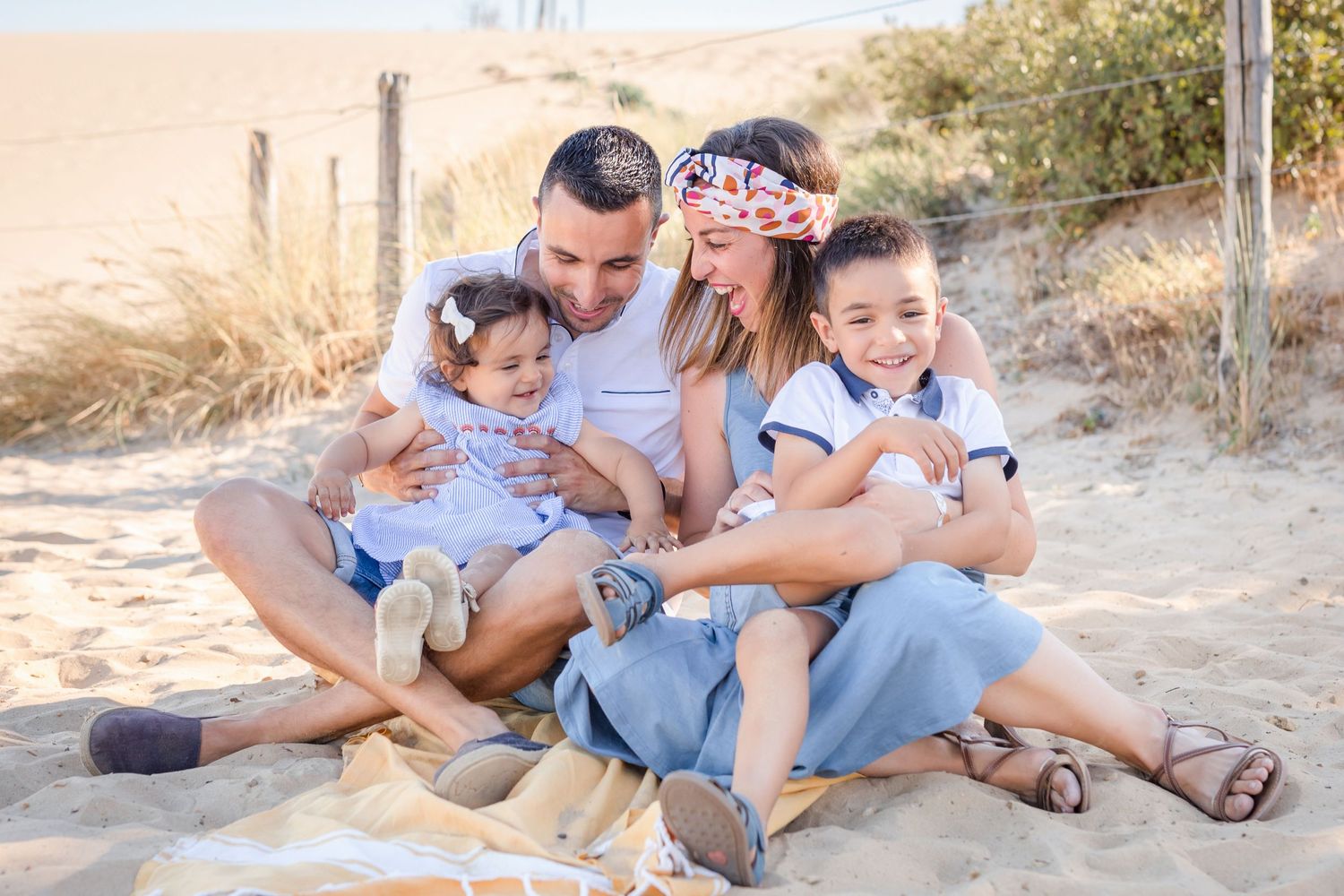 Family lounging together on sandy beach during sunset photoshoot.