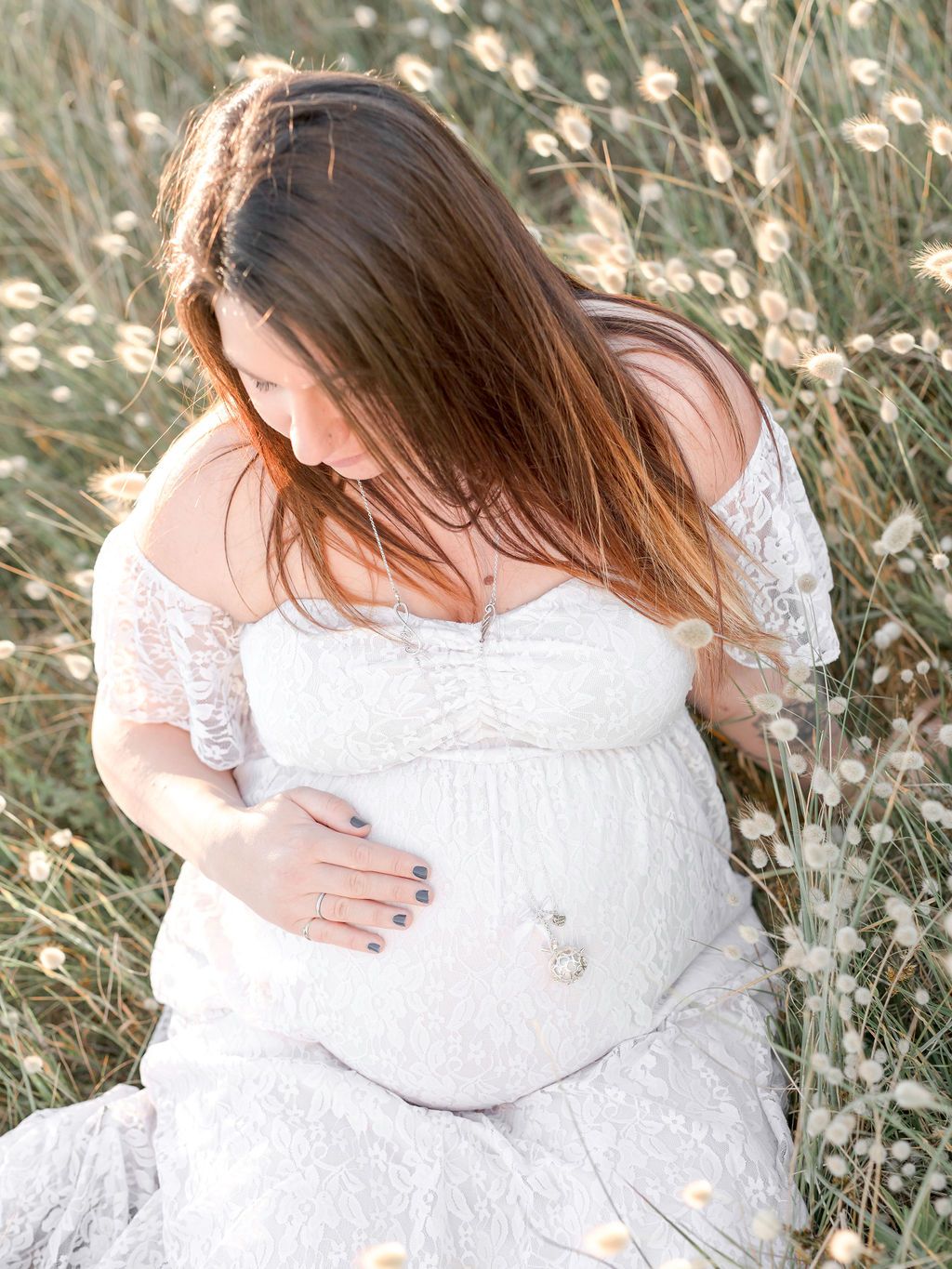 Someone wearing a flowing white lace dress sits gracefully in a sunlit meadow of flowers.