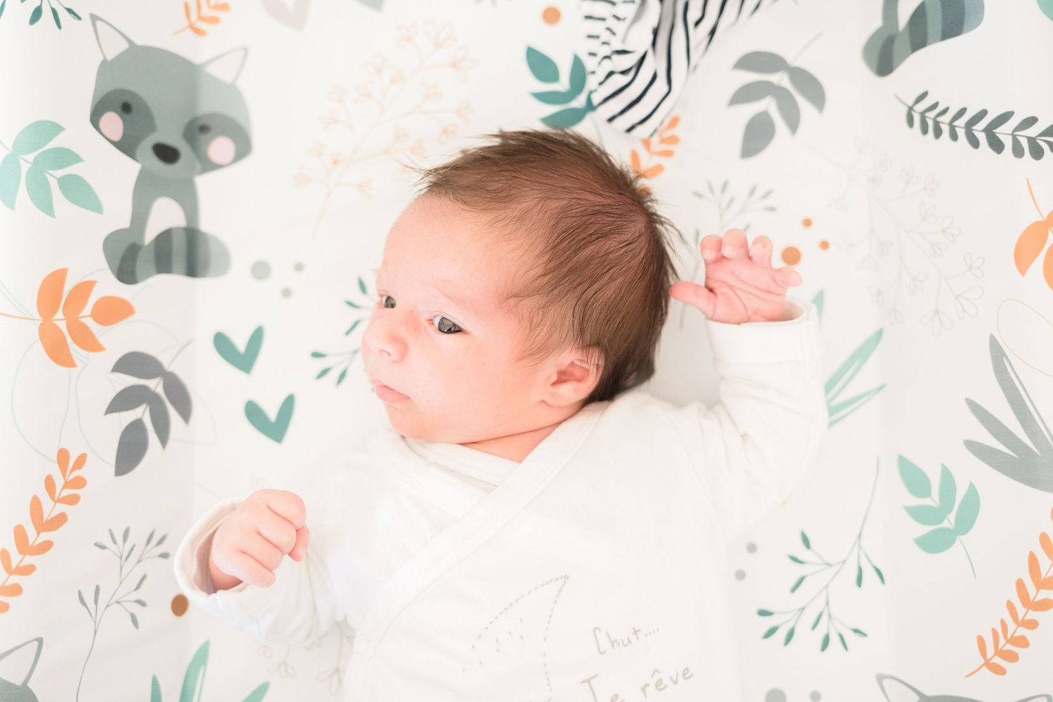 Infant lying on white blanket with decorative leaf and animal print pattern.