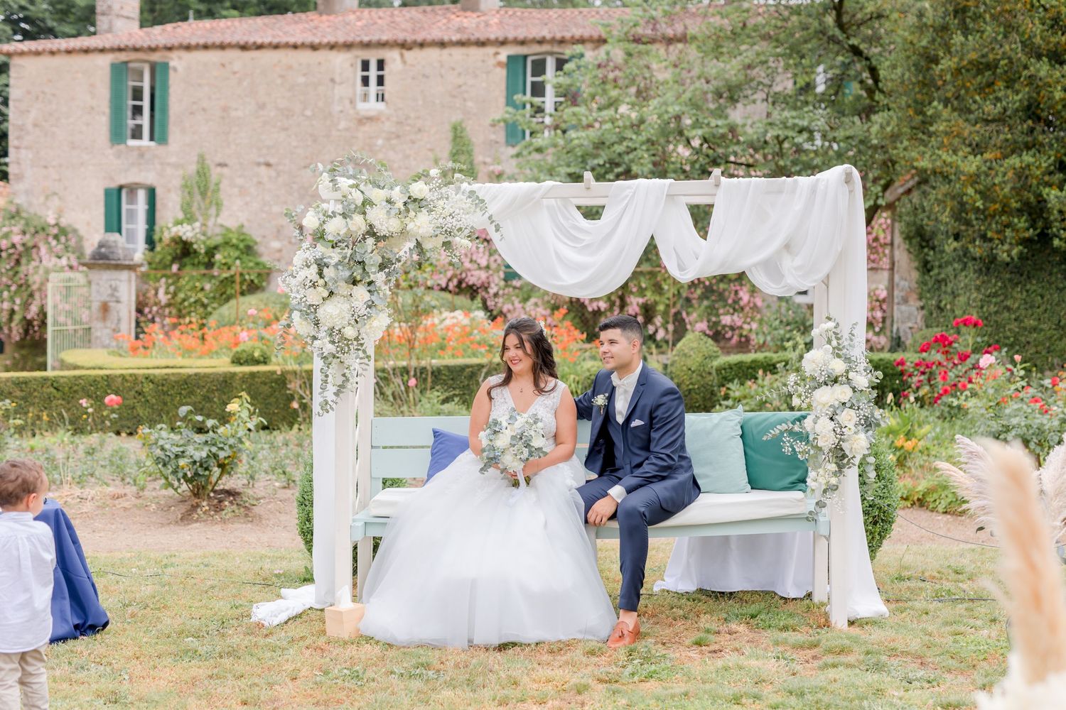 Wedding ceremony setup with white draped arch and seating in a garden setting.