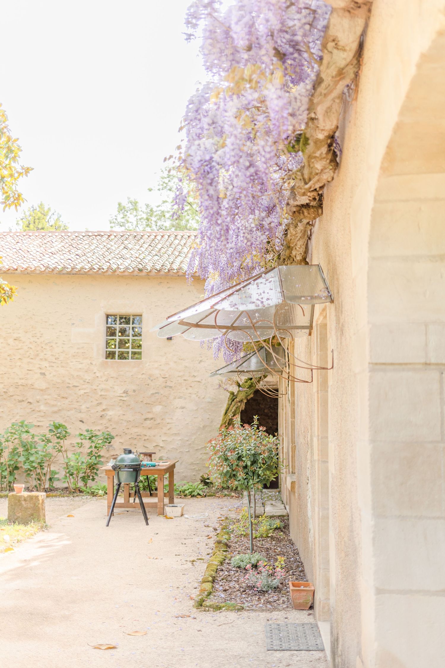 Charming stone archway with blooming wisteria vines frames a peaceful garden courtyard.